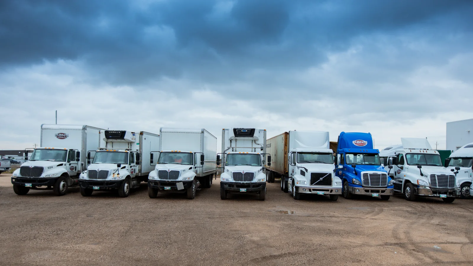 DBNS trucks lined up across the Winnipeg yard beneath a cloudy sky